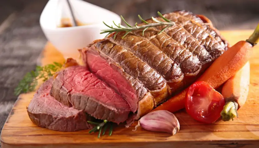 Un rôti de bœuf de 1k500, saignant et savoureux, servi avec des carottes, une tomate et de l'ail. Le temps de cuisson parfait pour ce délice.