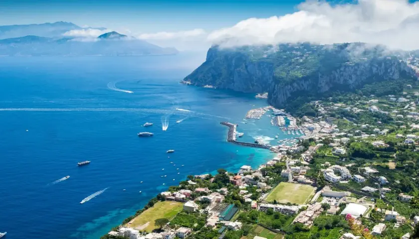 Widok na zatokę z łodziami i miasteczkiem na zboczu góry Capri.