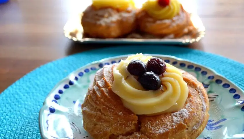 Zeppole, deliziosi dolci napoletani, guarnite con crema pasticcera e frutti di bosco su un piatto decorato.