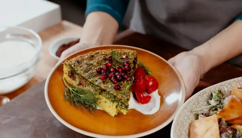 Une part de kuku sabzi, une tarte aux herbes persane, garnie de grenades et de tomates cerises, servie avec une touche de yaourt.