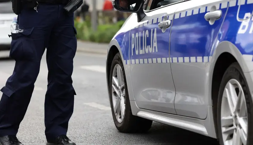 Policjant stoi obok radiowozu. Czy policja może zabrać telefon świadkowi? To pytanie nurtuje wielu.