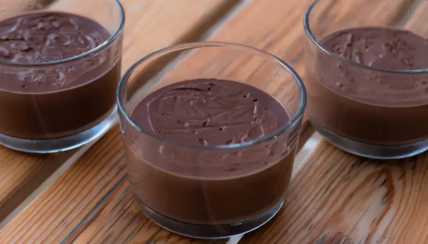 Tre glas med krämig, hemmagjord chokladpudding står på en träyta.