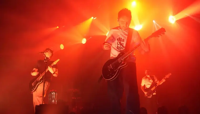 Koncert Myslovitz. Wokalista i gitarzysta na scenie, w tle basista. Czerwone światła podkreślają energię utworów.