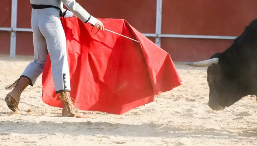 Torero con capote rojo se enfrenta a un toro bravo, evocando la tradición de los encierros más antiguos de España.