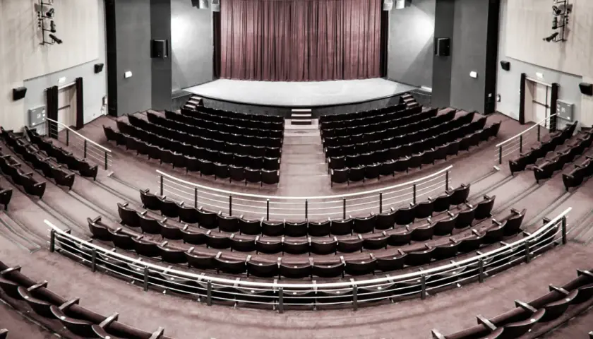 Pusta sala widowni w teatrze im. Aleksandra Sewruka w Elblągu, z rzędami czerwonych foteli i sceną w tle.