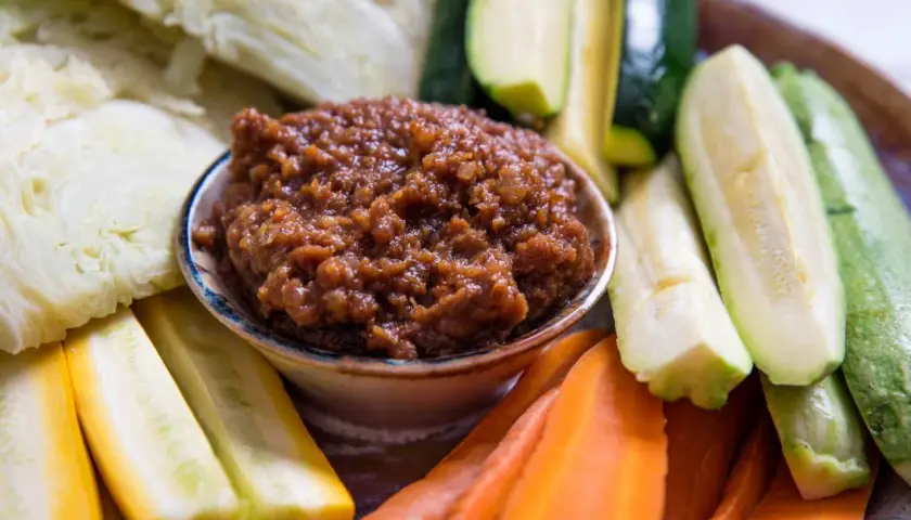 A bowl of savory miso dip is surrounded by fresh, colorful crudités: sliced zucchini, yellow squash, carrots, and cabbage wedges, ready for dipping.