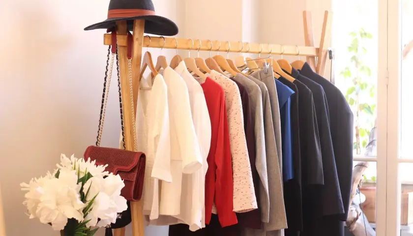 Un portant à vêtements avec un chapeau, des sacs et des vêtements. Une idée pour savoir comment arrêter d'acheter des vêtements.
