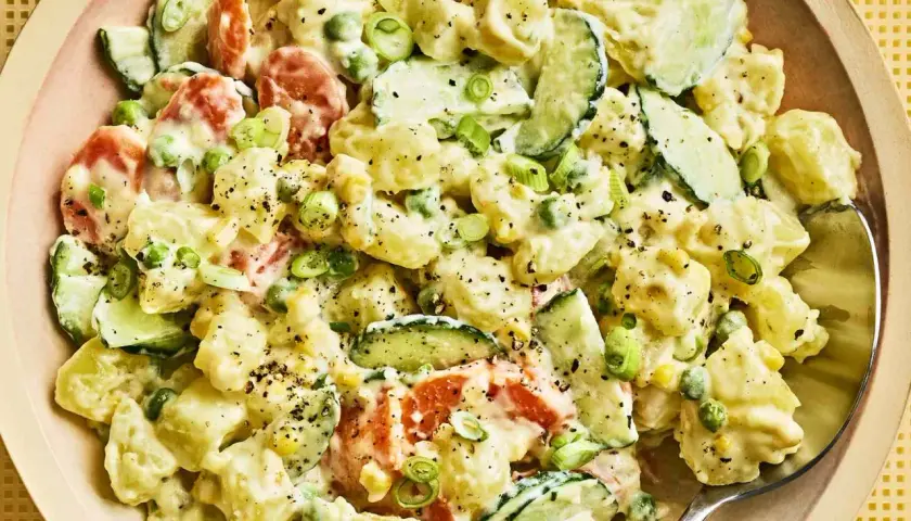 A creamy Japanese potato salad with chunks of potato, cucumber, peas, and carrots, garnished with green onions and black pepper.