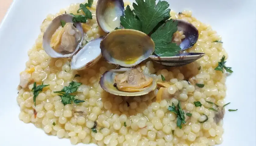 Piatto di fregola con vongole, profumata al prezzemolo e condita con un filo d'olio. Un classico della cucina sarda.