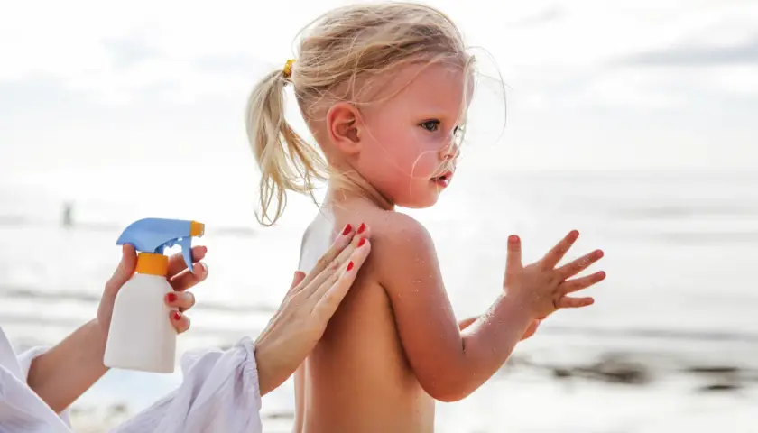 Ochrona przed słońcem jest kluczowa, by uniknąć oparzeń słonecznych u dzieci. Mama smaruje córkę kremem na plaży.