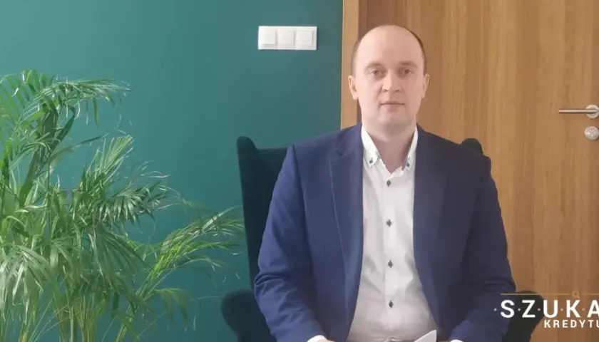 Mężczyzna w garniturze siedzi w fotelu obok rośliny.