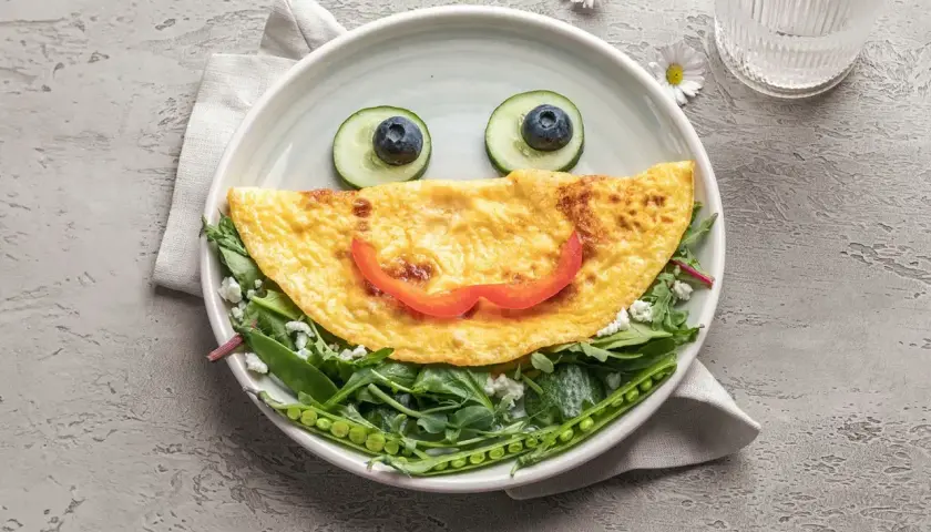 Uśmiechnięta omletowa buzia z oczami z ogórka i borówki, ułożona na sałatce z groszkiem. Idealny comfort food na dobry początek dnia.