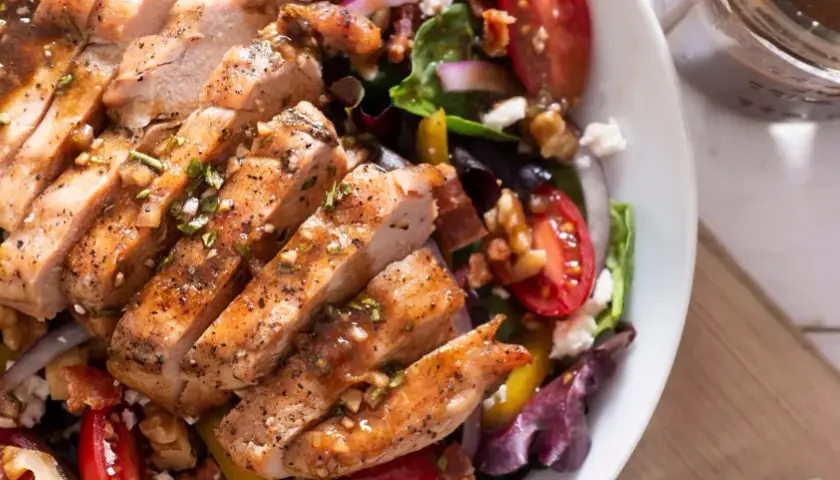 Deliziosa insalata estiva gourmet con pollo grigliato, pomodorini, noci e formaggio feta. Perfetta per un pasto leggero e saporito.