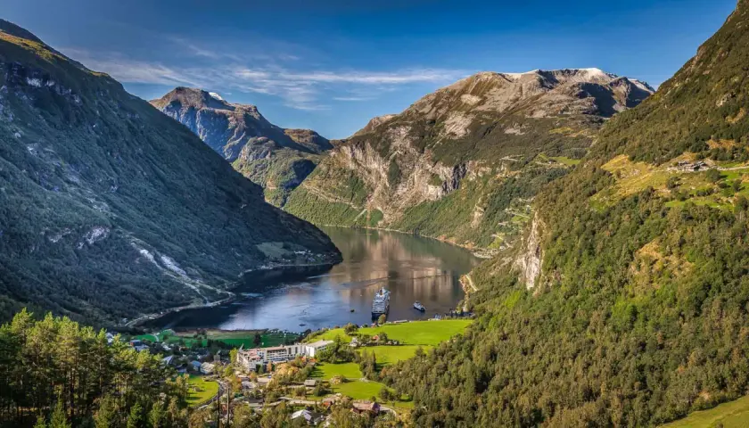 Majestätische fjorde norwegen, mit einem Kreuzfahrtschiff auf dem ruhigen Wasser, umgeben von steilen, grünen Bergen und einem kleinen Dorf.