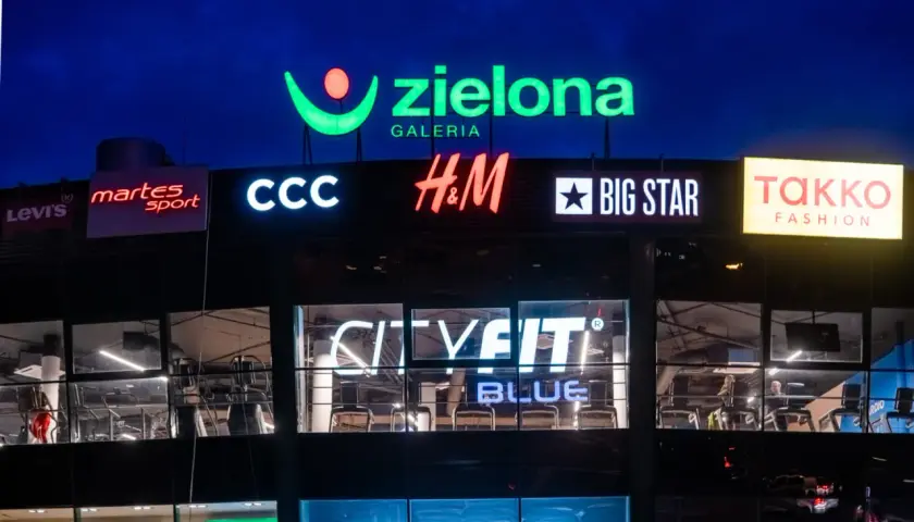 Nocny widok galerii handlowej z neonami sklepów: Zielona Galeria, CCC, H&M, Big Star, CityFit.