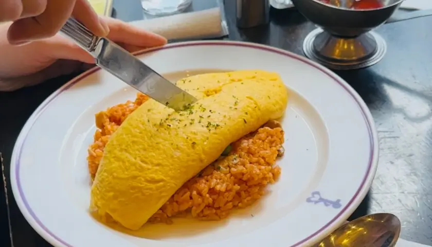 A knife cuts into a fluffy omelet atop rice, a delicious example of Japanese dishes with cheese.