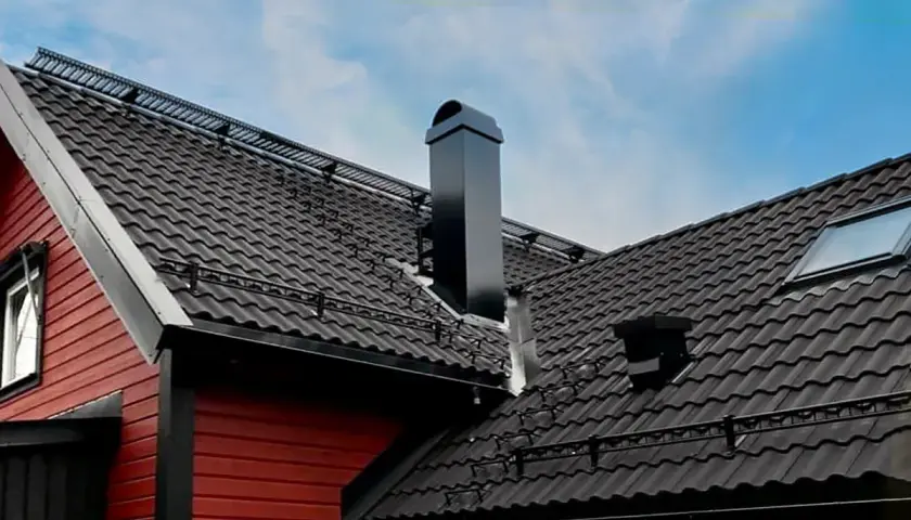 Svart, modern skorsten på ett tak med mörka takpannor. En röd träfasad syns till vänster.