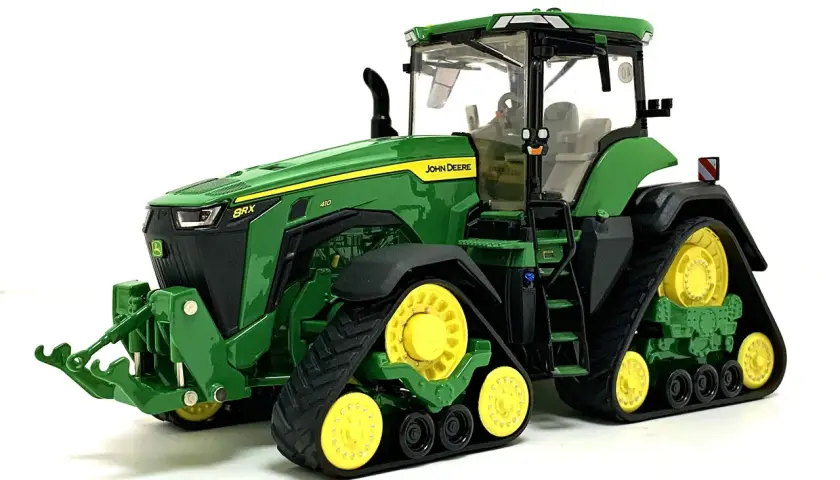 Zielony mini traktor John Deere z żółtymi kołami i gąsienicami, gotowy do pracy na farmie.