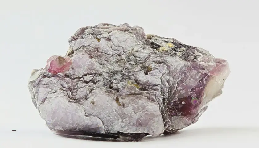 Ein schuppiger, lila-grauer Lepidolith-Stein mit glänzenden Oberflächen und einem kleinen, rosa Kristall.