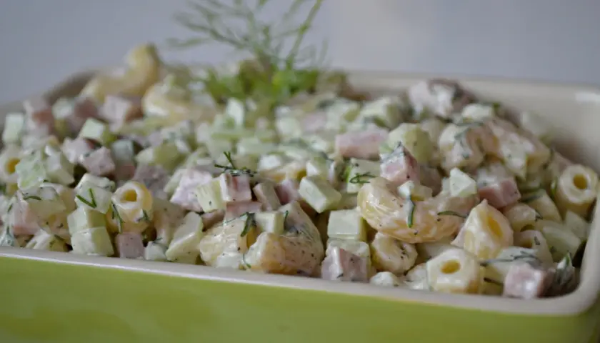 Pyszna sałatka z makaronem, szynką, ogórkiem i serem, udekorowana świeżym koperkiem.