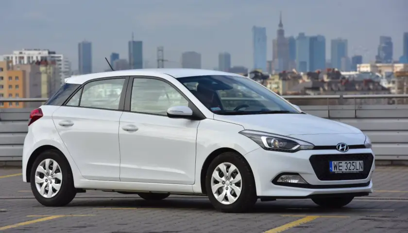 Biały Hyundai i20 zaparkowany na parkingu z widokiem na miasto w tle.