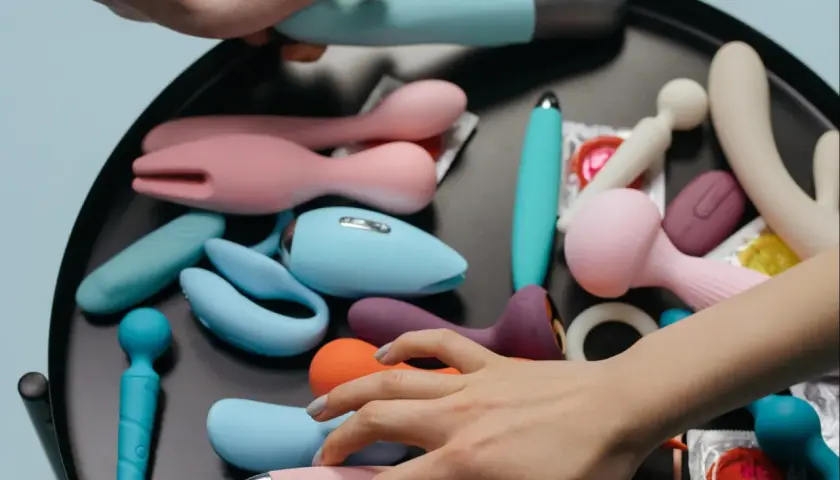 Mani che scelgono tra vari vibratori e sex toys, suggerendo la masturbazione femminile.