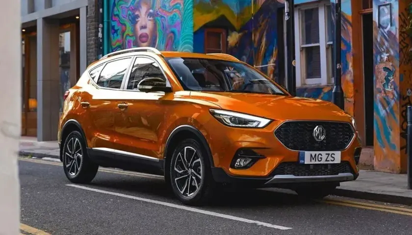Pomarańczowy MG ZS na tle kolorowego muralu. Sprawdź nasze samochody MG opinie i przekonaj się sam!