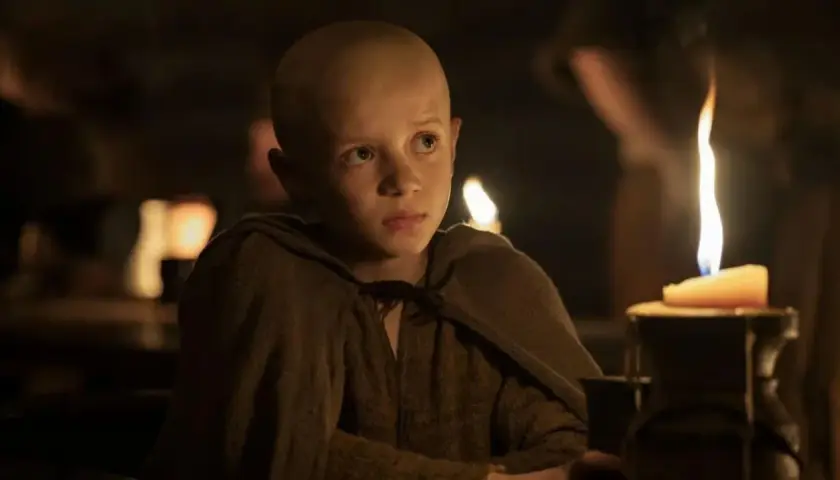 Un jeune garçon chauve, vêtu d'une tunique marron, regarde fixement une bougie allumée. Scène de "A Knight of the Seven Kingdoms Episode 3".