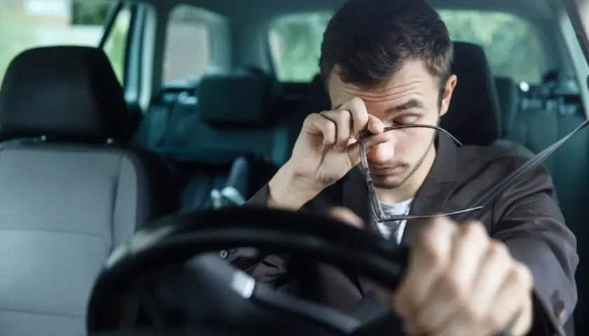 Hombre somnoliento se frota los ojos al volante, mostrando cómo el sueño y la fatiga influyen en la conducción.