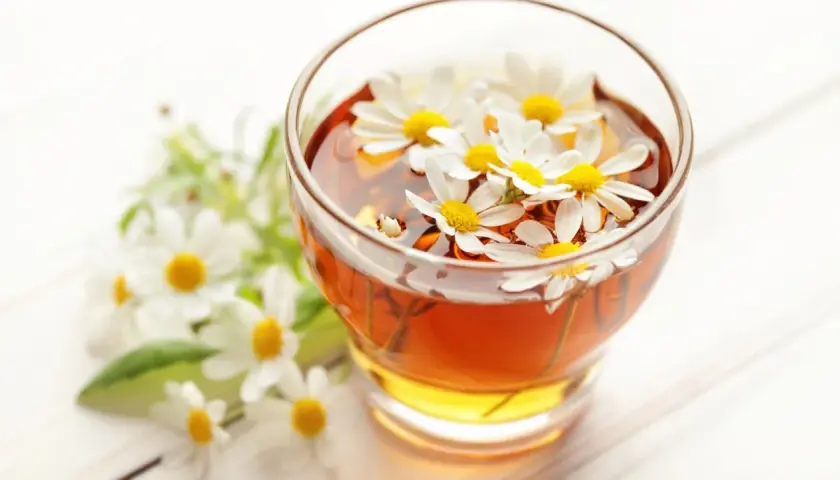 Un bicchiere di camomilla per bambini, con fiori freschi che galleggiano nella bevanda dorata.