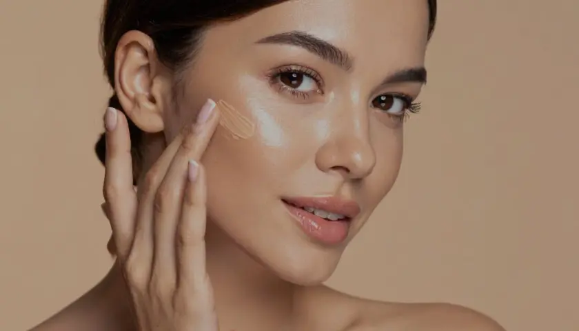 Donna applica fondotinta sul viso, un passo essenziale per capire come scegliere fondotinta perfetto per la tua pelle.