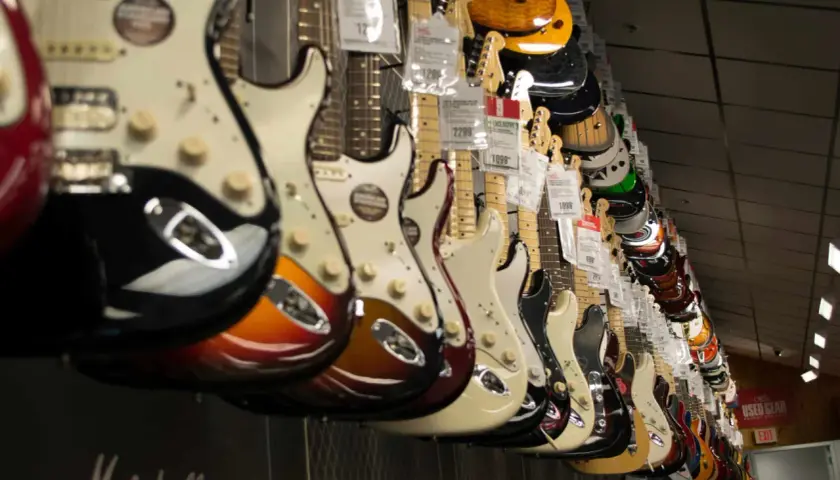Rząd gitar elektrycznych w sklepie, idealnych jako jaka gitara elektryczna na początek. Różne kolory i modele wiszą na ścianie.