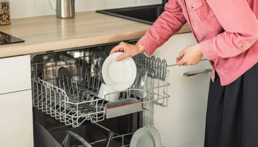 Kobieta wkłada talerz do zmywarki Bosch. Dowiedz się, ile prądu zużywa zmywarka Bosch, by oszczędzać energię.