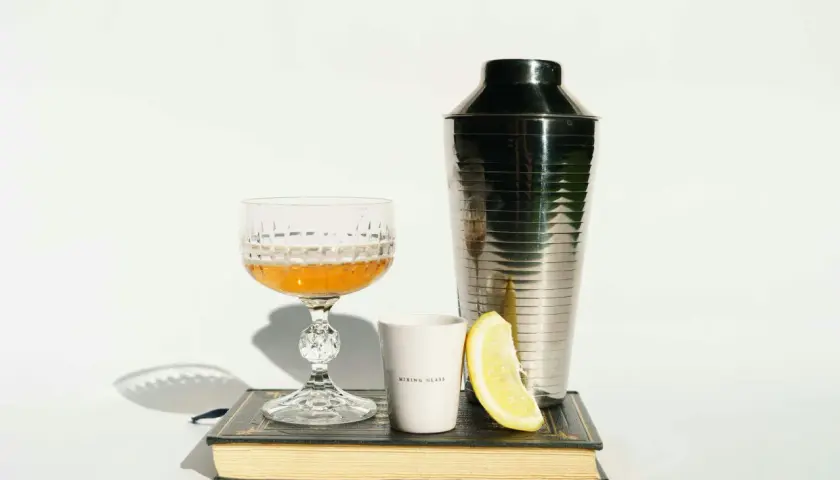 Szklanka z drinkiem, shaker, cytryna i książka. Idealne akcesoria, by dowiedzieć się, z czym pić amarula.