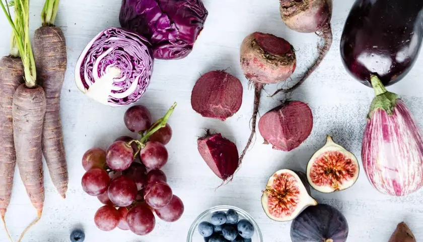 Un surtido de verduras raras y frutas moradas: zanahorias, col lombarda, remolachas, berenjenas, higos, uvas y arándanos.