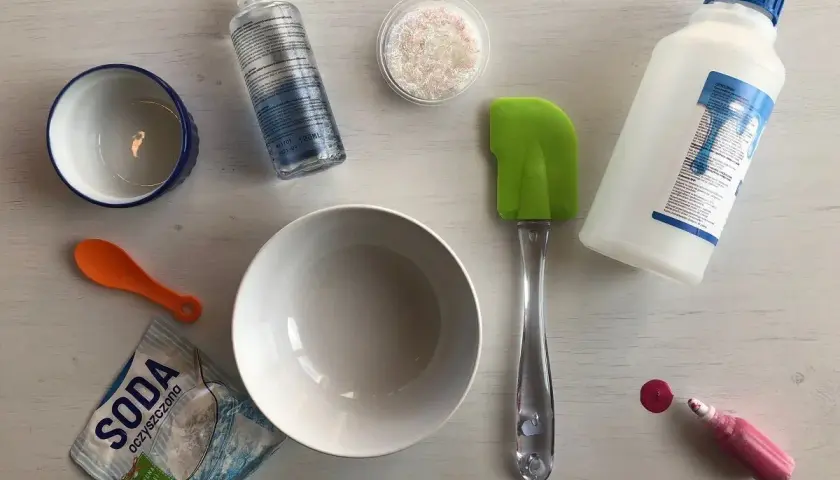 Składniki do zrobienia slime: klej, soda, boraks, brokat, miseczki, łyżeczka i szpatułka.
