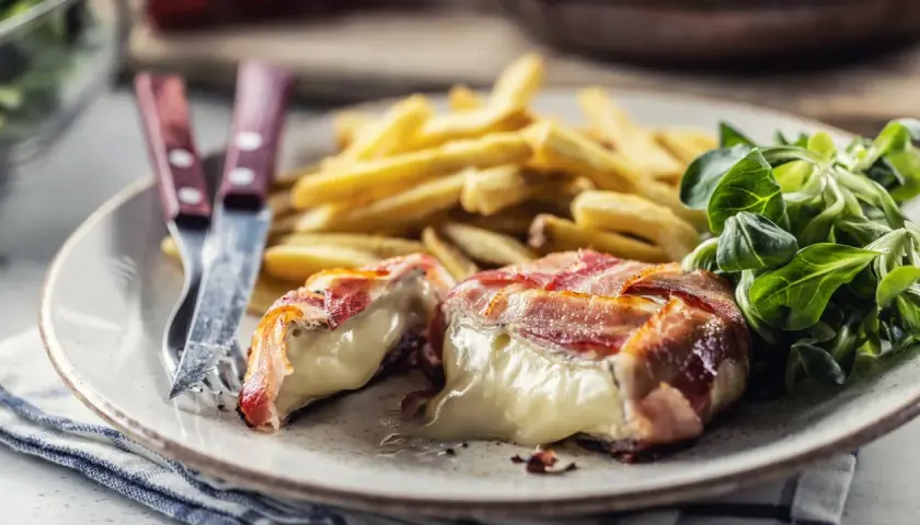 Ser camembert zawinięty w bekon, podany z frytkami i sałatką.