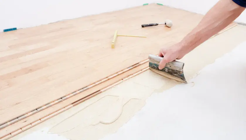 Pose d'un plancher bois étage : application de colle avec une spatule sur le support avant la pose des lames.