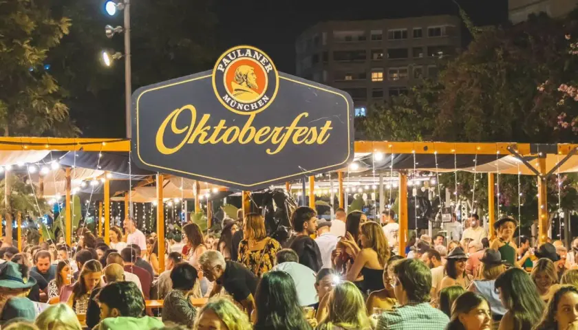 Gente disfrutando en un evento de Oktoberfest Valencia, con luces y un gran cartel de Paulaner.