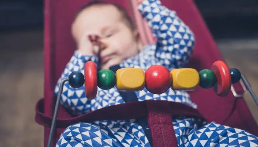Sover gott i sin babysitter elektrisk, med färgglada träpärlor som leksak.