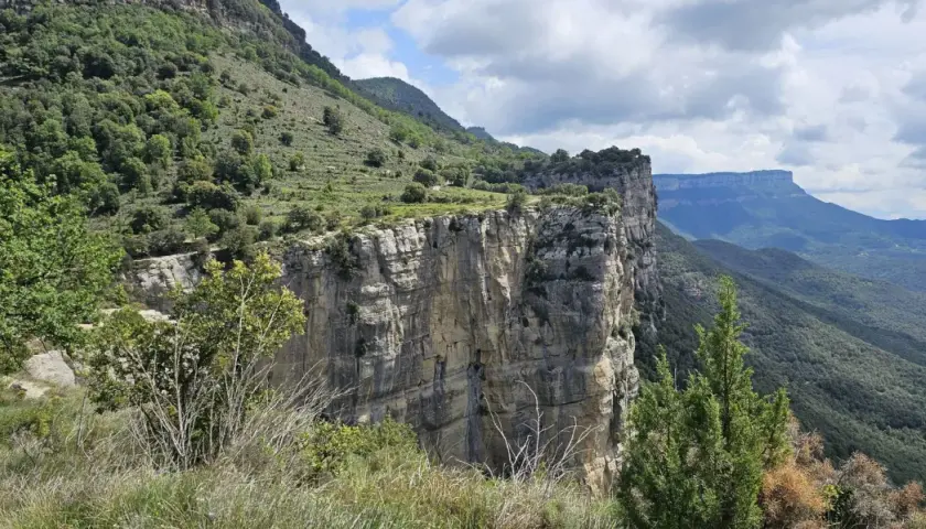 Impresionante pared rocosa del salt de sallent, con vegetación verde y un cielo nublado.