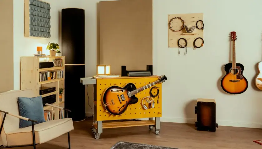 Kreative hobbykeller ideen: Gitarren, Kopfhörer und Kabel sind ordentlich an einer gelben Werkbank mit Lochwand befestigt. Akustikpaneele und weitere Instrumente schaffen eine musikalische Atmosphäre.