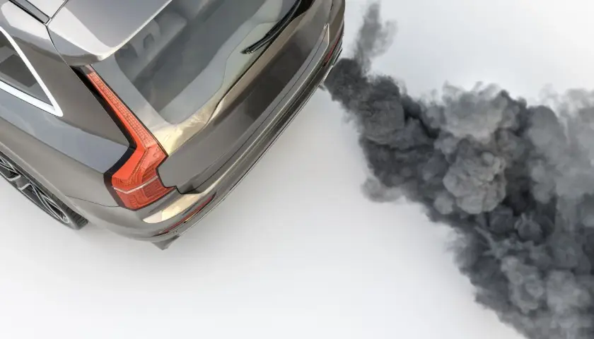 Un coche emite una densa nube de humo negro por el tubo de escape al acelerar, contaminando el aire.