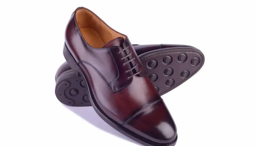 Eleganckie męskie buty ze skóry w kolorze koniaku. Widoczne różne rodzaje podeszwy w butach: skórzana i gumowa z charakterystycznym wzorem.