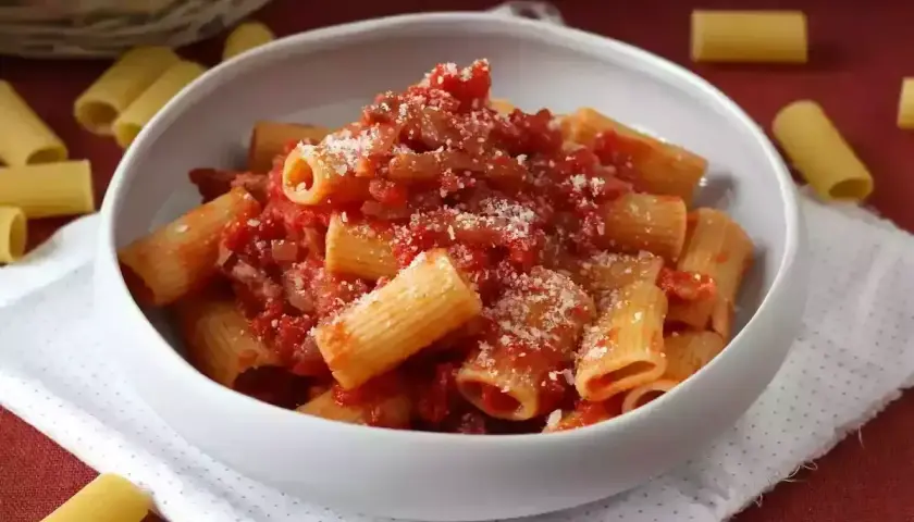 Pyszne rigatoni amatriciana, bogato polane sosem pomidorowym z guanciale i posypane parmezanem, w białej misce.