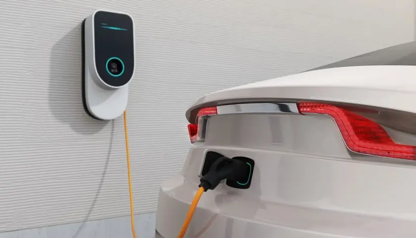 Nowoczesna stacja ładowania samochodów elektrycznych podłączona do białego auta. Sprawdź, jaka jest stacja ładowania samochodów elektrycznych cena.