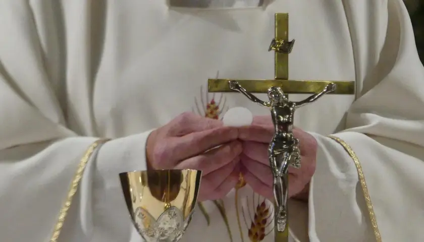 Ksiądz trzyma hostię i krzyż. Złoty kielich stoi obok. Zastanawiasz się, ile trwa msza?