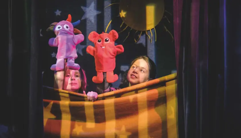 Två barn bakom en filt uppför dock teater med färgglada figurer.