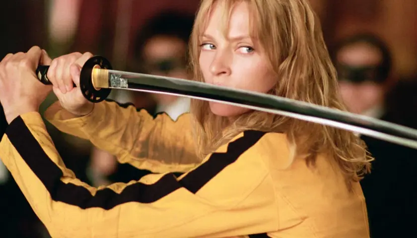 La Sposa, con la sua iconica tuta gialla, impugna la katana. Il suo sguardo è intenso, pronto a vendicarsi. Kill Bill: la benda sull'occhio è un monito.