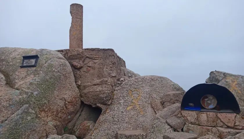 Cima del Puig de Cadiretes con un monolito, rocas y un pequeño refugio con un objeto en su interior.